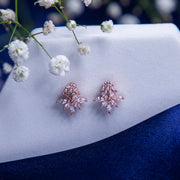 A pair of rose gold-colored prismatic studs earrings placed on a blue fabric with white floral accents.